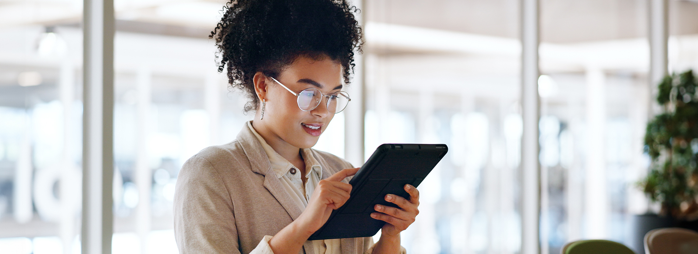A young woman with curly hair and glasses using a tablet.